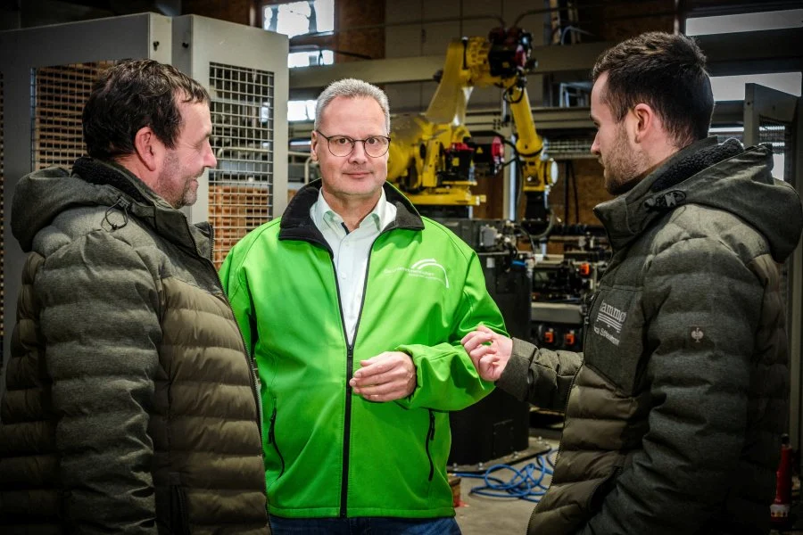 Arne Bär lacht mit zwei Handwerkern in einer Werkhalle