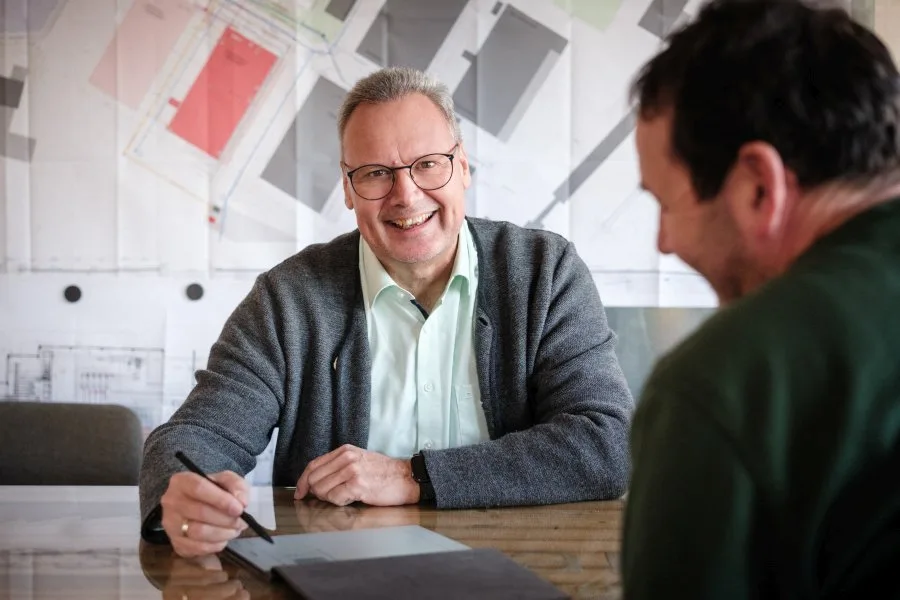Arne Bär lacht am Besprechungstisch im Gespräch mit einem Handwerker
